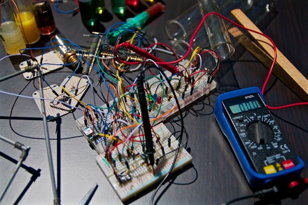 A breadboard wired with jumper leads, next to a multimeter on a workbench